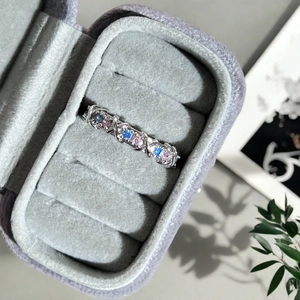 Macro d'une bague croisée en argent avec zircons roses et bleus dans un écrin en velours
