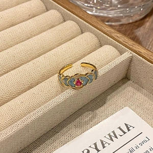 Detail van vintage emaille ring met rode robijn en blauwe bloemmotieven op een displayblad