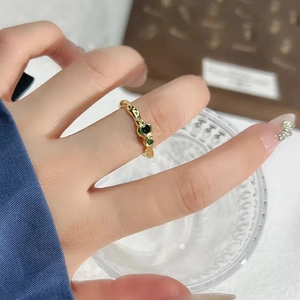 Onregelmatige gouden open ring met drie groene zirconen om de vinger gedragen