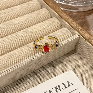 Detail van vintage gouden ring met rode steen en blauwe accenten op houten dienblad