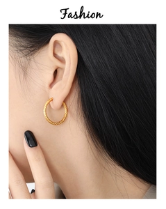 Detalle de pendientes de aro dorados con textura tejida usados por una modelo