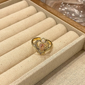 Detail van een vintage kroonring met roze edelsteen en parel op beige linnen textuur