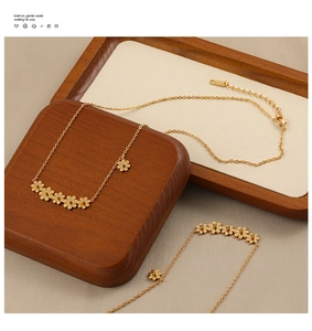 Detail of a gold titanium steel necklace featuring multiple daisy flower charms on a tray