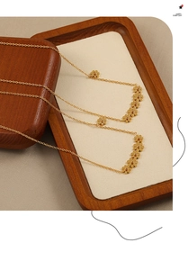 Close-up of golden stainless steel necklace with delicate daisy flower charms on soft padding