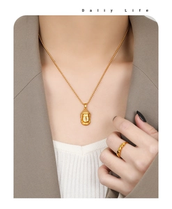 Détail d'un collier pendentif bouddha en or mat et bague minimaliste portés par un mannequin