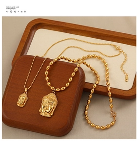 Détail de deux pendentifs tête de Bouddha dorés avec différents styles de chaînes sur plateau