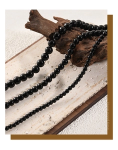 Detail of three black onyx bead necklaces in various sizes on natural stone and wood