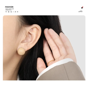 Nahaufnahme eines minimalistischen beigen Ohrrings und eines goldenen Kordelrings