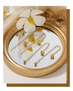 Close-up of golden heart threader earrings with fine chains on a mirror surface