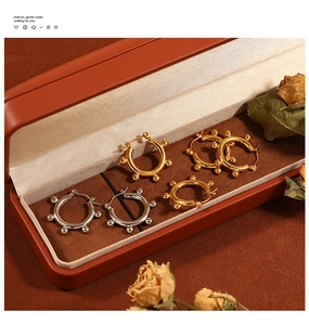 Detailed close-up of golden and silver bean hoop earrings on leather jewelry case