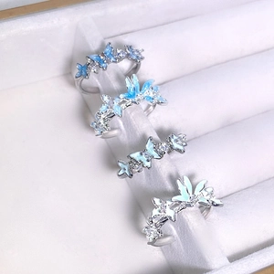 Détail de quatre bagues réglables en émail papillon et fleurs avec cristaux en boîte à bijoux