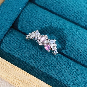 Macro shot of silver ring with pink zircon heart and rose petals in a velvet jewelry box