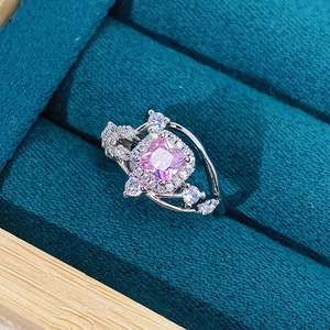 Macro shot of square pink gemstone ring with halo diamonds on dark teal velvet box