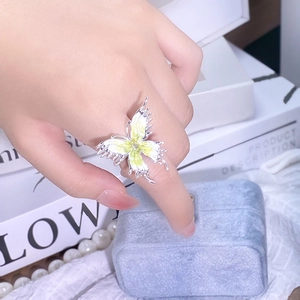 Détail d'une bague papillon argentée avec émail jaune et vert sur le doigt d'un modèle