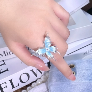 Gros plan d'une bague papillon en émail bleu clair sur le doigt avec des perles