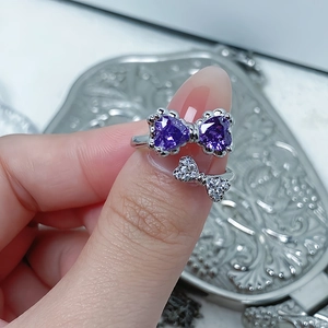 Detail showing hand wearing a double bow ring with purple heart-shaped cubic zirconia stones