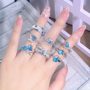 Dettaglio di anelli con zirconi blu mare sulle dita con design a cuore e geometrici