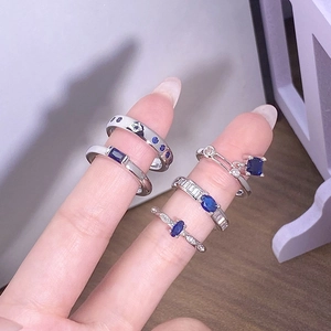 Dettaglio di cinque anelli argentati con zirconi blu mare indossati su dita modella