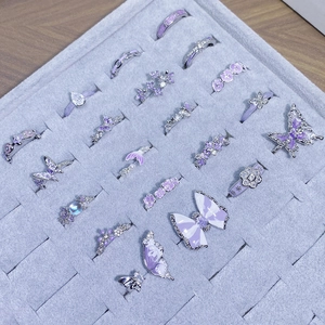 Set dettagliato di anelli in smalto viola con fiori e farfalle in una scatola regalo
