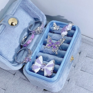 Dettaglio di anelli in smalto viola con fiori e farfalle in una scatola di velluto