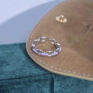 Dettaglio macro di un anello a catena in argento con smalto viola su tessuto verde