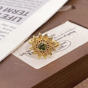 Macro shot of gold sunflower ring featuring a green zircon center and carved petals