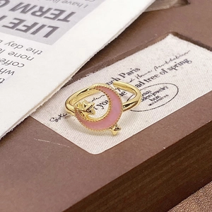 Detail of gold-plated crescent moon and star ring with pink enamel on vintage paper