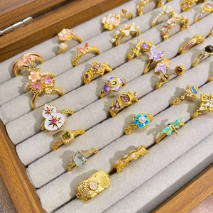 Bagues dorées style palais vintage avec fleurs et papillons émaillés dans une boîte grise