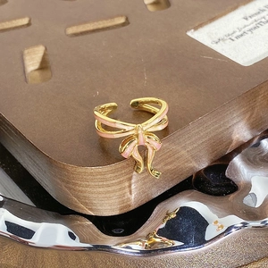 Gros plan détaillé d'une bague nœud dorée vintage avec émail rose sur support bois