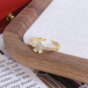 Gros plan d'une bague dorée avec fleur en émail blanc, perles et détails en zircon