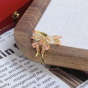 Vue macro d'une bague vintage dorée avec nœud en émail rose sur plateau en bois