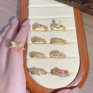 Close-up of vintage floral enamel rings with butterfly details and pearls in a display case