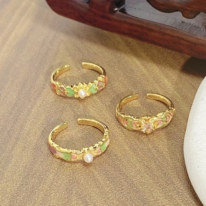 Close-up of three vintage enamel flower rings with pearls and gold-plated details