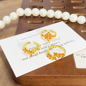 Close-up of vintage gold flower rings with orange enamel and small crystals on a card
