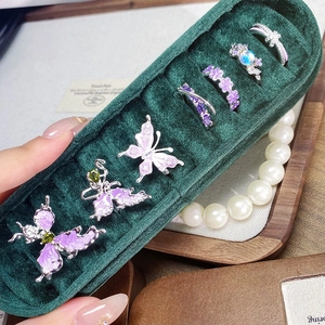 Dettaglio di anelli con farfalla in smalto viola e fiori con zirconi in scatola