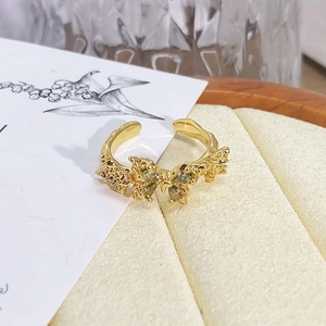 Detail of vintage golden butterfly ring with olive green gems and lava texture