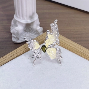 Dettaglio macro dell'anello a farfalla con gemma verde e petali di fiori smaltati