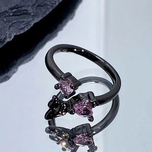 Gros plan d'une bague punk noire avec pierres de cœur roses et motif chat