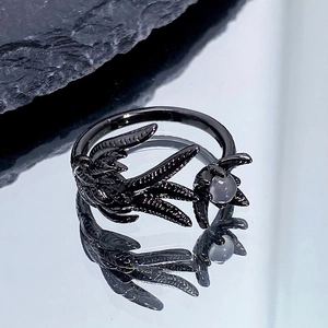 Détail d'une bague punk feuilles sombres avec perle grise sur fond de pierre noire