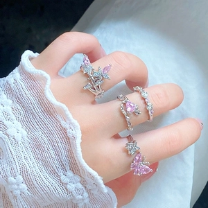 Detailed view of four silver-plated rings with pink zircons and butterfly motifs on fingers