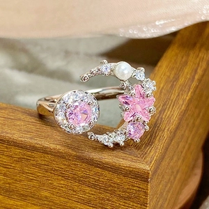 Detail of pink zircon moon and star open ring with pearl on a wooden texture background