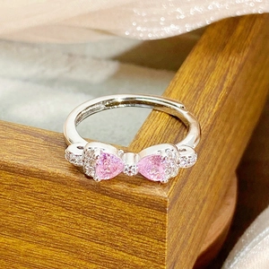 Macro shot of silver bow ring with pink heart zircons and pavé diamonds on silk