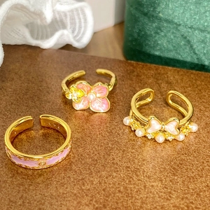 Détail de bagues dorées avec fleurs en émail rose, perles et zircons brillants