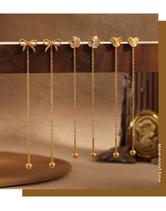 Detail of three gold titanium steel threader earrings with bow, flower, and heart motifs