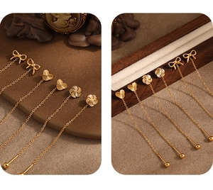 Close-up detail of gold titanium steel ear threads featuring bow, heart, and windmill charms.