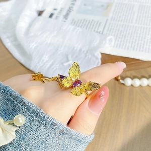 Détail d'une bague papillon dorée avec pierre violette sur dentelle et perles