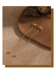 Detail of gold bow earrings with long hanging tassels on a premium brown display stand