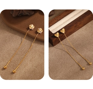 Detail of gold titanium tassel earrings with heart and flower motifs on wood stand