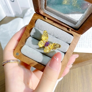 Détail macro d'une bague papillon dorée avec pierre violette dans un coffret luxe