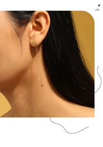 Close-up of elegant gold flower threader earrings with a long tassel and metallic ball charm
